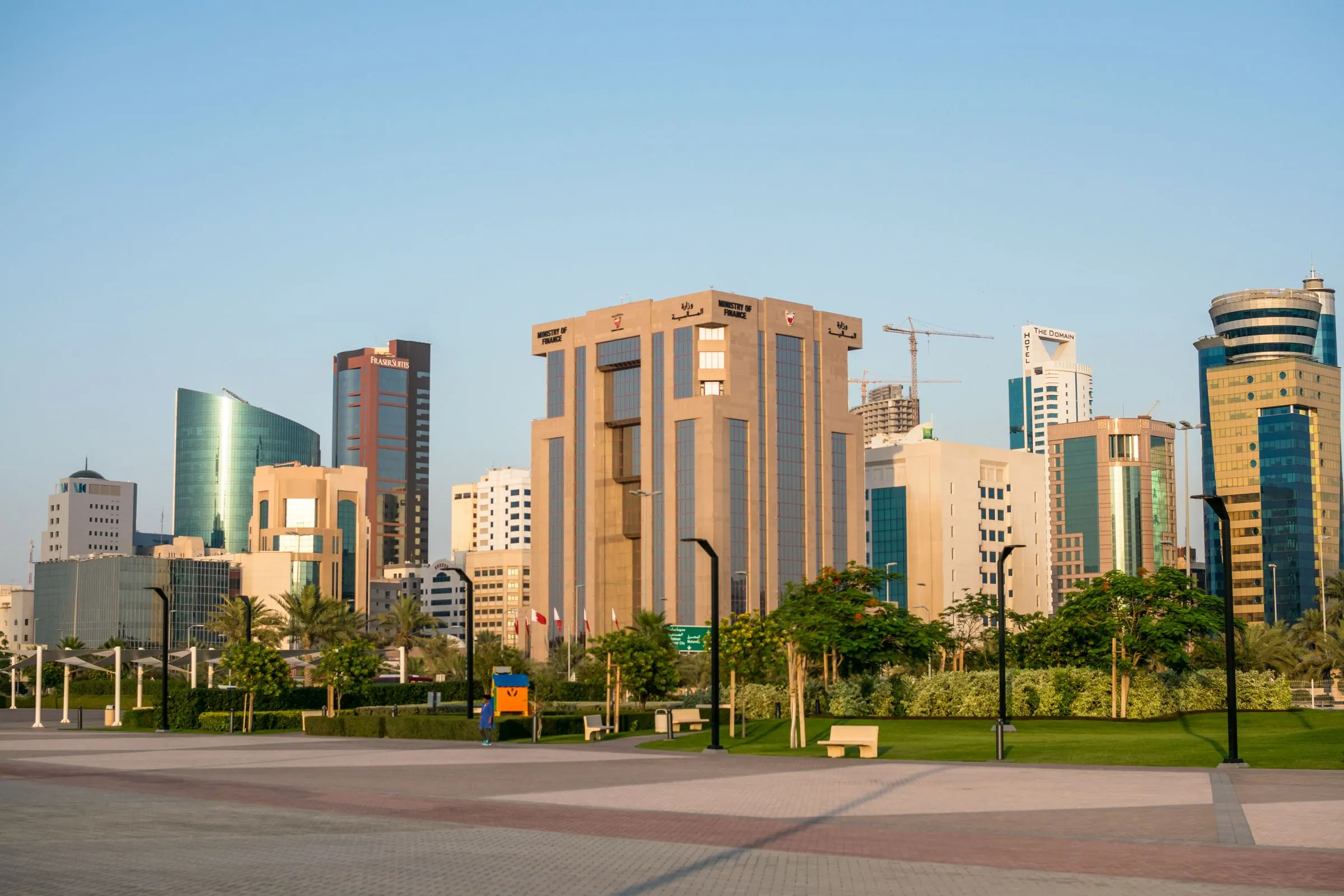Manama modern belvárosa napsütésben, pálmafákkal és üvegtornyokkal, Bahrein